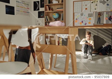 Lonely and unhappy schoolboy sitting on the floor of empty classroom Lonely and unhappy schoolboy sitting on the floor of empty classroom 95837809