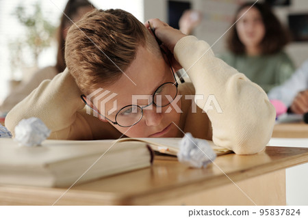 Offended and upset schoolboy bending over desk to protect his head 95837824
