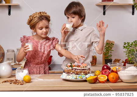 Little friends are making a cake together at a kitchen against a white wall with shelves on it. Little friends are making a cake together at a kitchen against a white wall with shelves on it. 95837825