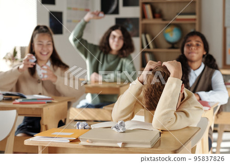 Discriminated schoolboy covering his head while defending from classmates 95837826