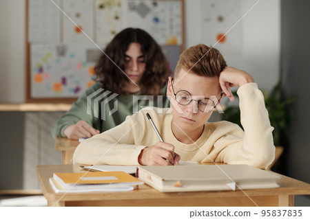 Clever youthful schoolboy making notes in copybook during individual assignment Clever youthful schoolboy making notes in copybook during individual assignment 95837835