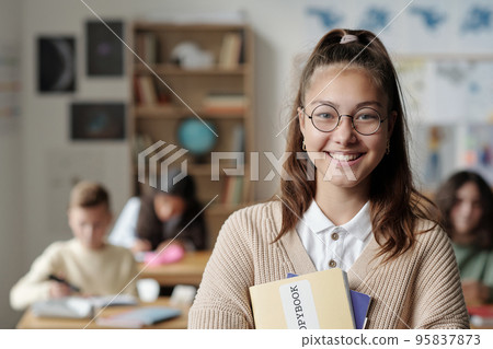 Smiling youthful schoolgirl in eyeglasses and casualawear looking at camera Smiling youthful schoolgirl in eyeglasses and casualawear looking at camera 95837873