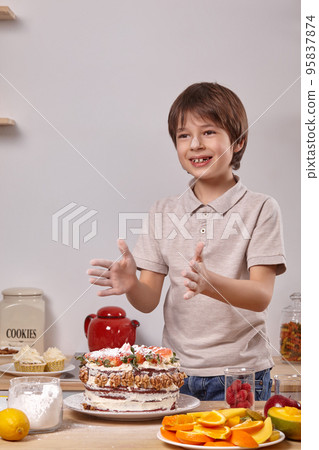 Little boy is making a homemade cake with an easy recipe at kitchen against a white wall with shelves on it. Little boy is making a homemade cake with an easy recipe at kitchen against a white wall with shelves on it. 95837874