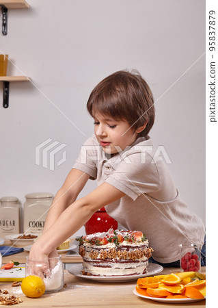Little boy is making a homemade cake with an easy recipe at kitchen against a white wall with shelves on it. Little boy is making a homemade cake with an easy recipe at kitchen against a white wall with shelves on it. 95837879