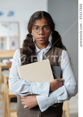 Serious youthful schoolgirl in smart casualwear standing in front of camera 95837889