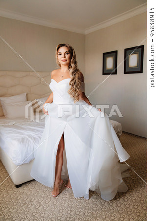 the morning of the bride. a barefoot blonde in a white dress in a bedroom. 95838915
