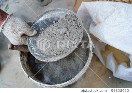 men's gloved hands sift through the sand for the cement mortar.  95838930