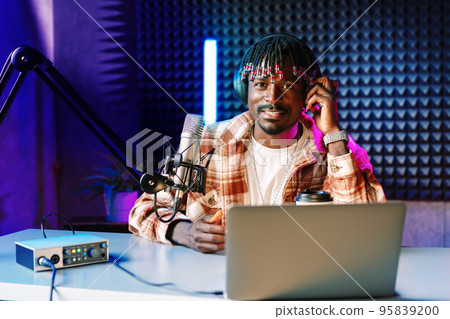 African radio host sitting at desk recording in studio with microphone and laptop African radio host sitting at desk recording in studio with microphone and laptop 95839200