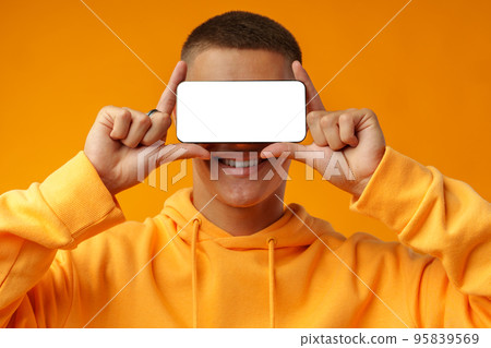 Smiling young man showing mobile phone blank white screen on yellow background Smiling young man showing mobile phone blank white screen on yellow background 95839569