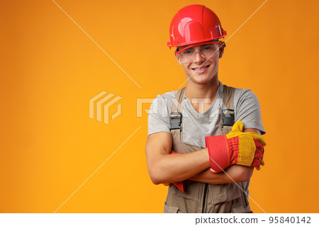 Young construction worker in helmet and uniform posing on yellow background in studio 95840142