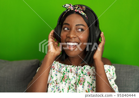 African woman listening to music with headphones while sitting on couch at home 95840444