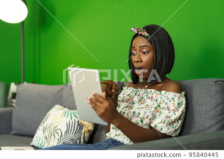 Young African woman using digital tablet while resting at home Young African woman using digital tablet while resting at home 95840445