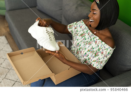 African young woman sit on couch at home unpack cardboard box with online purchase 95840466