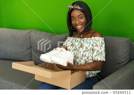 African young woman sit on couch at home unpack cardboard box with online purchase African young woman sit on couch at home unpack cardboard box with online purchase 95840511