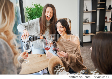Young women enjoying winter weekends inside contemporary barn house. Four girls having fun and drinking wine. 95840547
