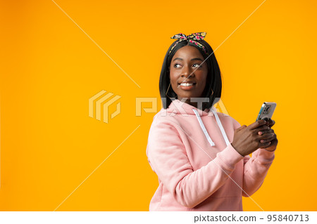 Happy african girl using her smartphone against yellow background. Happy african girl using her smartphone against yellow background. 95840713