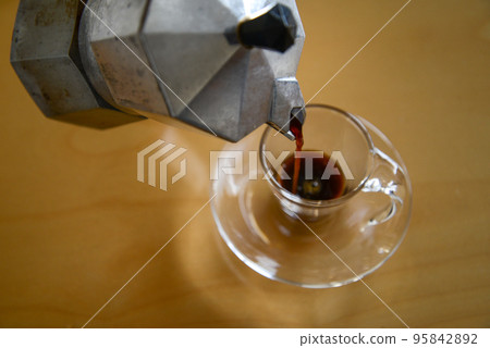 Pouring espresso brewed in a moka pot into a glass demitasse cup Pouring espresso brewed in a moka pot into a glass demitasse cup 95842892