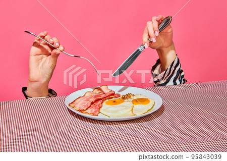 Female hands with fork and knife eating English breakfast with fried eggs and bacon Female hands with fork and knife eating English breakfast with fried eggs and bacon 95843039