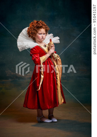Portrait of little red-headed girl, child in image of royal person with serios face and hot-dog isolated over dark green background 95843197