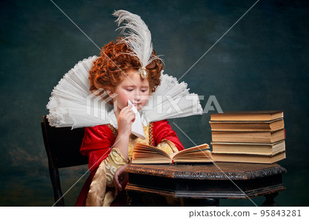 Portrait of little red-headed girl, child in costume of royal person reading book isolated over dark green background Portrait of little red-headed girl, child in costume of royal person reading book isolated over dark green background 95843281