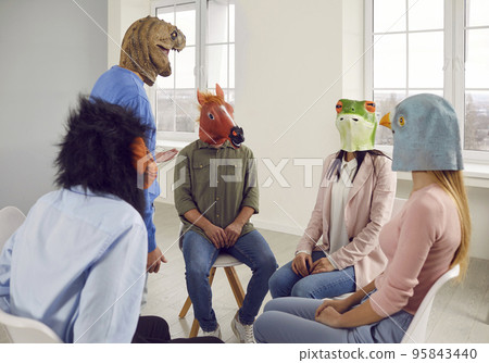 Conversation of young people in rubber masks on their heads during support group meeting. 95843440