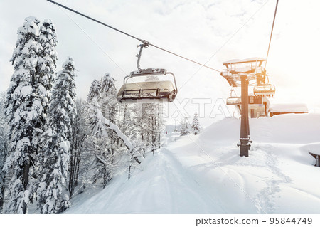 Ski lift empty ropeway on hilghland alpine mountain winter resort on bright sunny evening . Ski chairlift cable way with people enjoy skiing and snowboarding. Sunset sky backlit shining on background 95844749