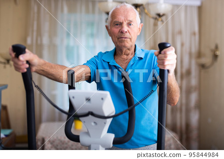 Senior man with elliptical trainer at home Senior man with elliptical trainer at home 95844984