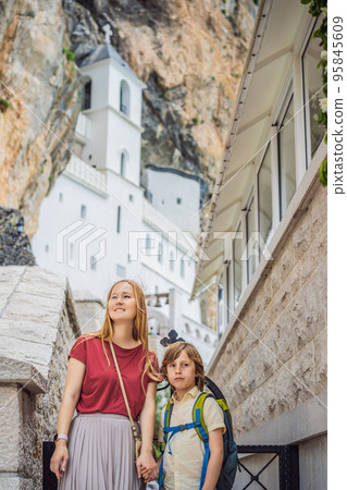 Mother and son tourists in Monastery of Ostrog, Serbian Orthodox Church situated against a vertical background, high up in the large rock of Ostroska Greda, Montenegro. Dedicated to Saint Basil of Mother and son tourists in Monastery of Ostrog, Serbian Orthodox Church situated against a vertical background, high up in the large rock of Ostroska Greda, Montenegro. Dedicated to Saint Basil of 95845609