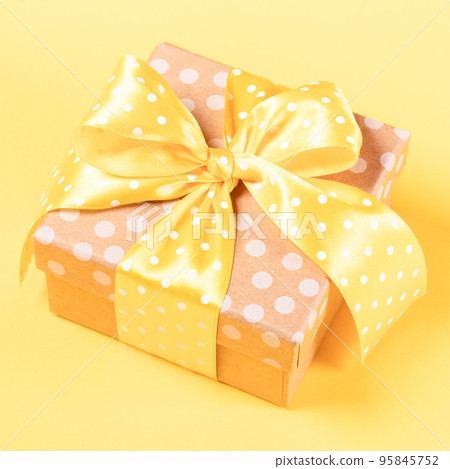 One gift box wrapped by polka dot craft paper with yellow polka dot bow on yellow background. Present box for any holiday. Close up. Square shot. One gift box wrapped by polka dot craft paper with yellow polka dot bow on yellow background. Present box for any holiday. Close up. Square shot. 95845752