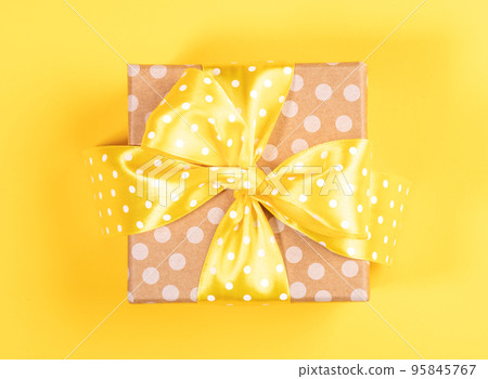 One wrapped polka dot craft gift box with yellow polka dot bow on yellow background. Minimal image for any holiday, shopping and sales. Top view. Close up. 95845767