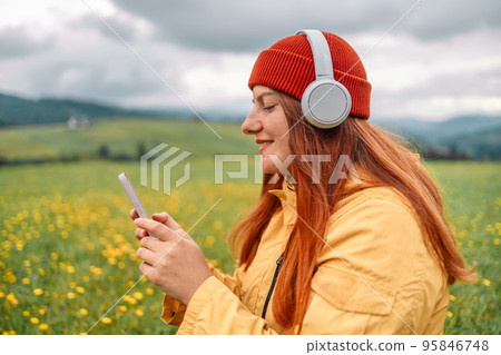 Caucasian beautiful woman wearing red hat and casual clothes, smiling with happiness, adventure traveling alone and hiking on the top of mountains, listening to music and enjoying nature in summer Caucasian beautiful woman wearing red hat and casual clothes, smiling with happiness, adventure traveling alone and hiking on the top of mountains, listening to music and enjoying nature in summer 95846748