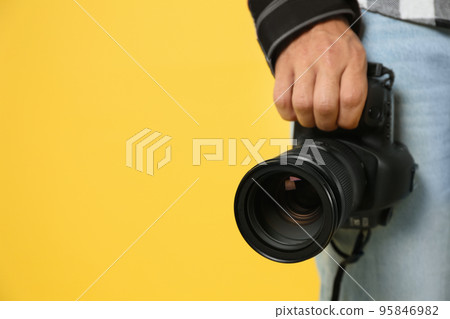 Professional photographer with modern camera on yellow background in studio, closeup. Space for text 95846982