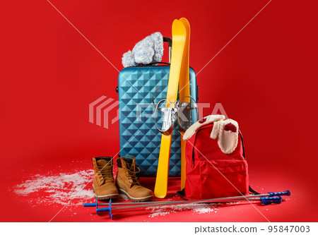 Suitcase with warm clothes and skis on red background. Winter vacation Suitcase with warm clothes and skis on red background. Winter vacation 95847003