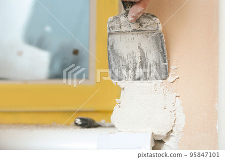 Man plastering window area with putty knife indoors, closeup. Interior repair Man plastering window area with putty knife indoors, closeup. Interior repair 95847101