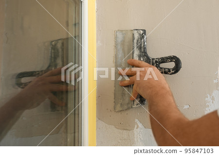 Man plastering window area with putty knife indoors, closeup. Interior repair Man plastering window area with putty knife indoors, closeup. Interior repair 95847103