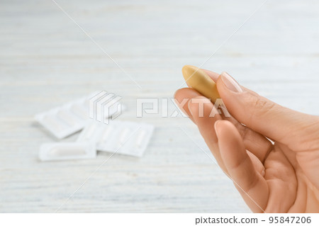 Woman holding suppository at white wooden table, closeup. Hemorrhoid treatment Woman holding suppository at white wooden table, closeup. Hemorrhoid treatment 95847206