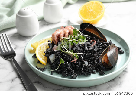 Delicious black risotto with seafood on white marble table Delicious black risotto with seafood on white marble table 95847309