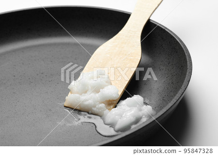 Frying pan with coconut oil and wooden spatula on white background, closeup. Healthy cooking 95847328