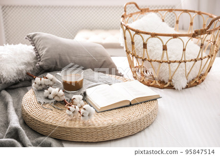 Composition with cup of drink, cotton and book on wicker pouf indoors 95847514