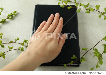 Female hand on Bible and twigs on light textured background Female hand on Bible and twigs on light textured background 95847620