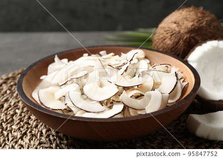 Tasty coconut chips in bowl on wicker mat Tasty coconut chips in bowl on wicker mat 95847752