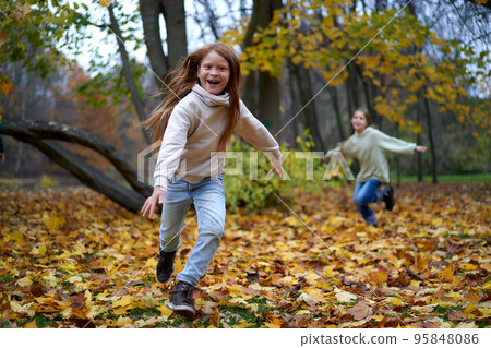 Brother and sister are running around the autumn park with their arms spread out like the wings of airplanes. Children are playing and laughing, having fun in a public park.Copy space for your design. 95848086