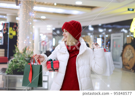 A cheerful woman walks around the mall with shopping as a gift for the Christmas holidays. Festive boxes and bags with gifts in the hands of a person. Xmas is coming 95848577