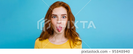Headshot Portrait of happy ginger red hair girl with funny face looking at camera. Pastel blue background. Copy Space 95848940