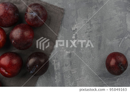 Several blue plums on a gray concrete background. One plum rolled off. Ripe autumn plums on the background. Copy space.  95849163