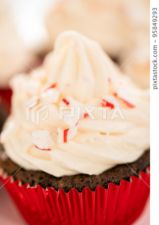 Freshly baked chocolate cupcakes with peppermint frosting and decorating with crushed peppermint candy cane candies. 95849293