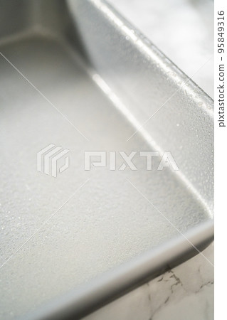 Greasing metal square baking pan to bake sweets. Greasing metal square baking pan to bake sweets. 95849316
