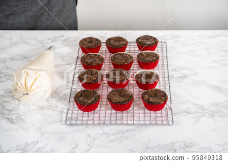 Piping peppermint buttercream frosting on top of the chocolate cupcakes and decorating with crushed peppermint candy cane candies. Piping peppermint buttercream frosting on top of the chocolate cupcakes and decorating with crushed peppermint candy cane candies. 95849318