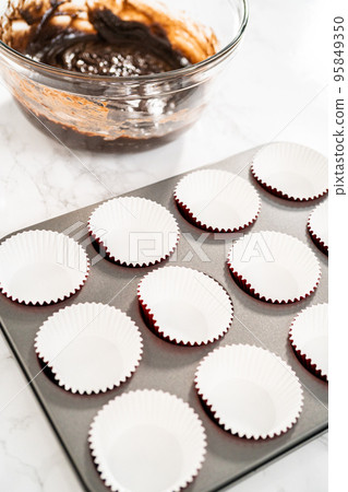 Scooping cake batter with dough scoop into cupcake foil liners to bake chocolate peppermint cupcakes. Scooping cake batter with dough scoop into cupcake foil liners to bake chocolate peppermint cupcakes. 95849350