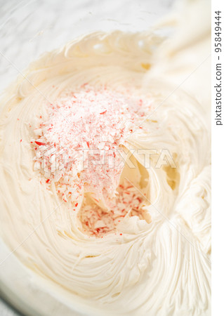 Whisking buttercream frosting in a glass mixing bowl with an electric hand mixer to prepare the peppermint buttercream frosting. Whisking buttercream frosting in a glass mixing bowl with an electric hand mixer to prepare the peppermint buttercream frosting. 95849444